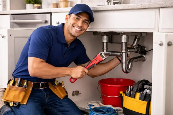 a plumber smiling at the camera while fixing a kitechen sink from 24 Hr Plumbing Leander in Leander, TX - Kitchen Sink Leaks Repair